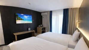 Habitación de hotel con dos camas, un escritorio, un televisor en la pared y una ventana con cortinas.