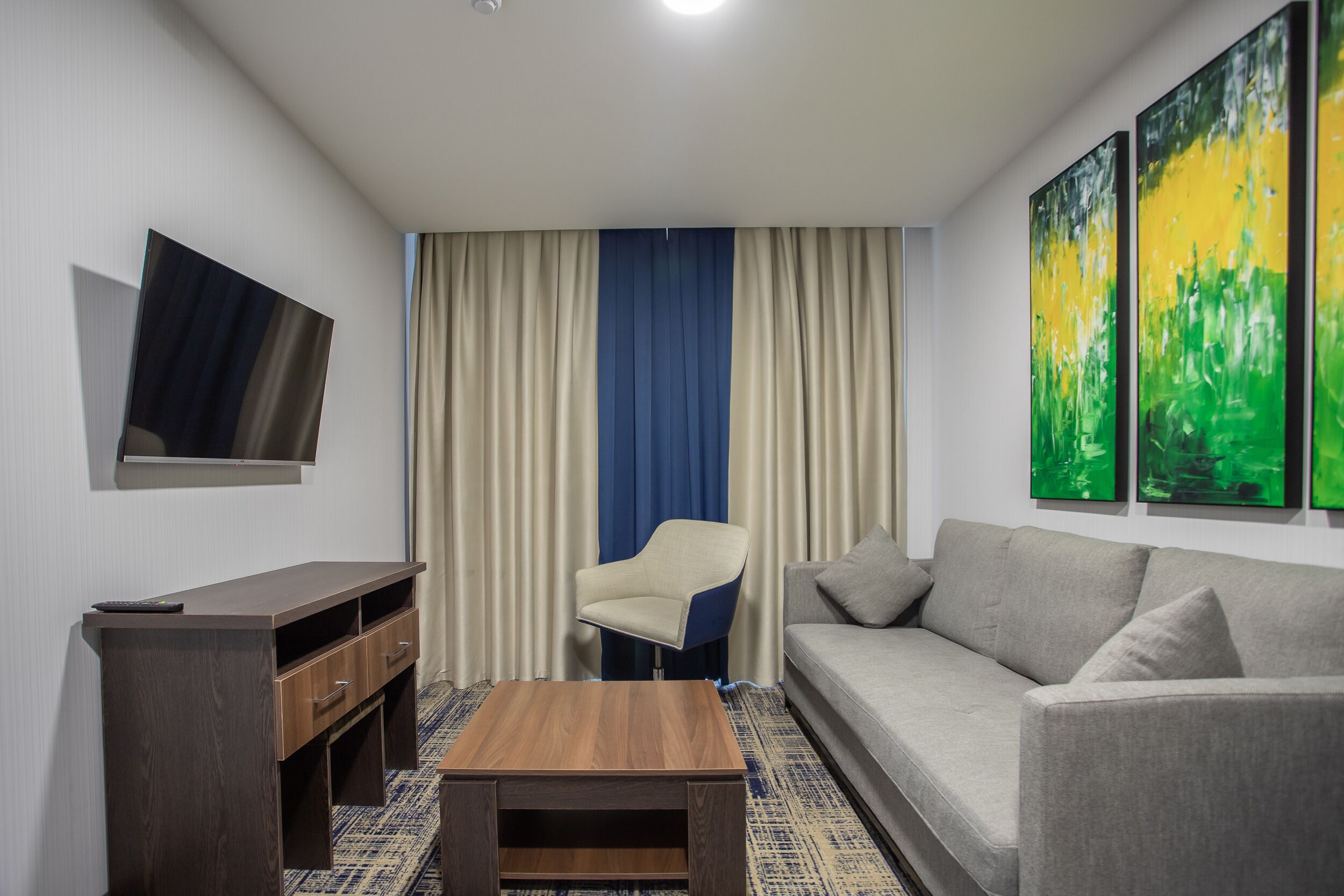 A modern living room with a sofa, a coffee table, a TV mounted on the wall, and a chair.