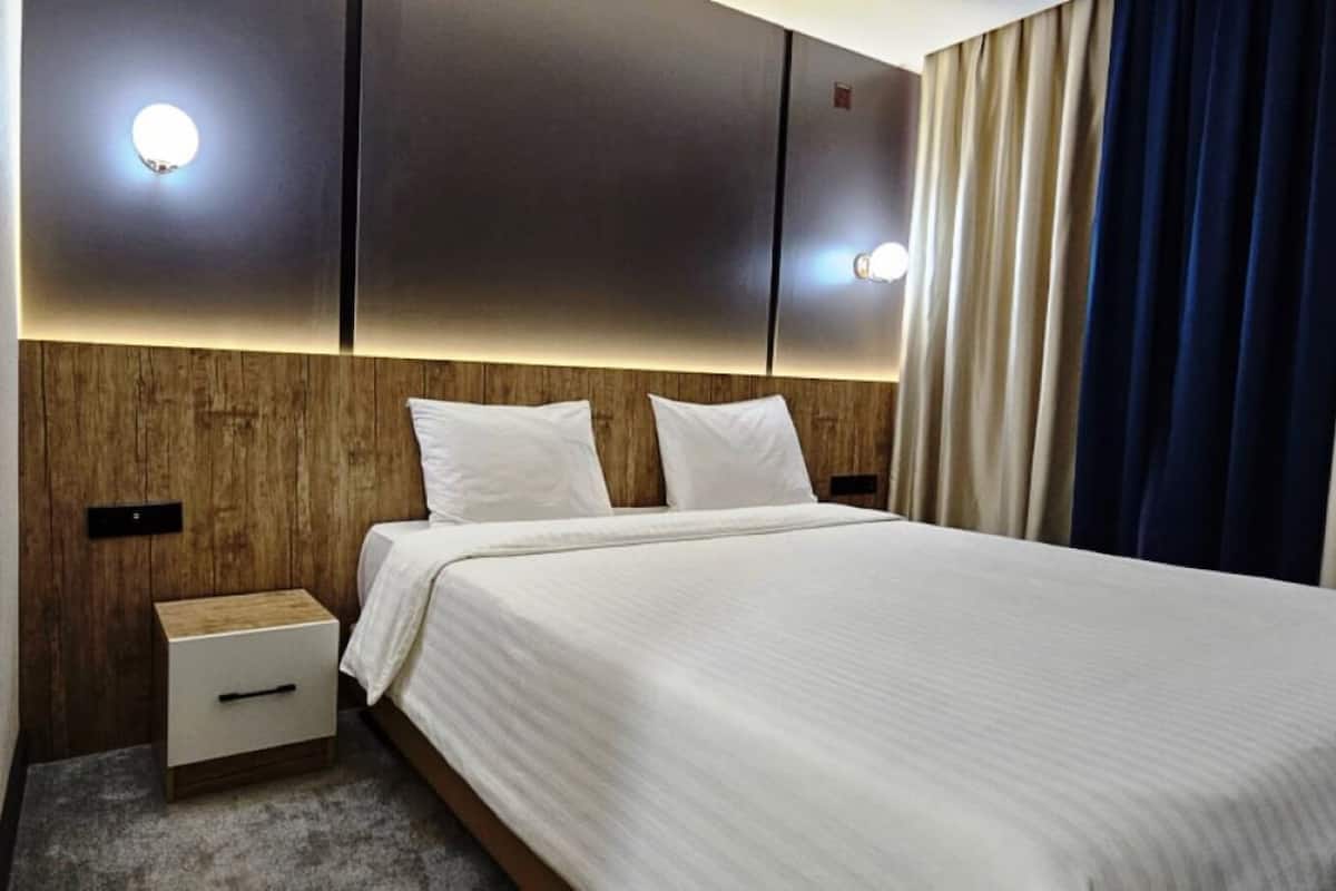 Una habitación de hotel con cama, mesita de noche y luces fijadas a la pared.