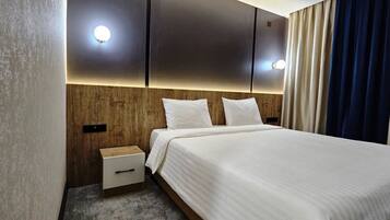 A hotel room with a bed, bedside table, and wall-mounted lights.