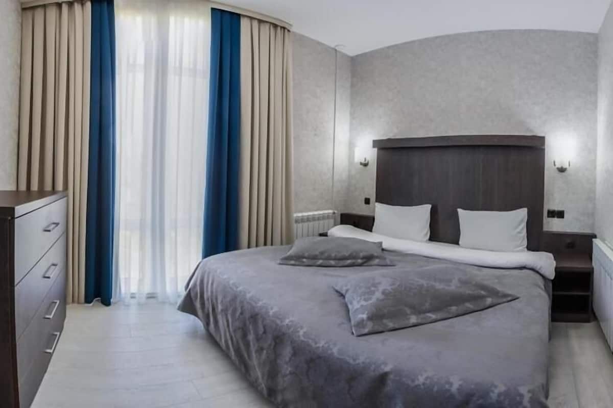 Una habitación de hotel moderna con una cama grande, un aparador y una ventana con cortinas.