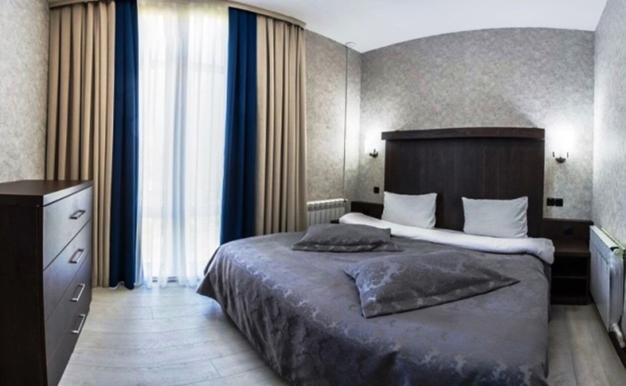 Una moderna camera d'albergo con un letto grande, una cassettiera e vista sull'esterno dalla finestra.