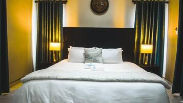 A hotel room with a large bed, two bedside lamps, a clock on the wall, and curtains on the windows.