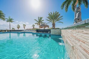 Une piscine d’un bleu éclatant, avec des chaises longues, des palmiers et une statue en pierre.