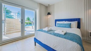 A hotel room with a large sliding glass door leading to a pool area, a bed with a blue headboard, and a white textured bedspread.