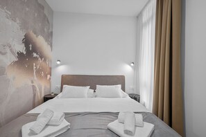 A hotel room with a large bed, two bedside tables, a wall with a textured mural, and a window with curtains. - Enjoy Suites & Apartments (Zagreb)
