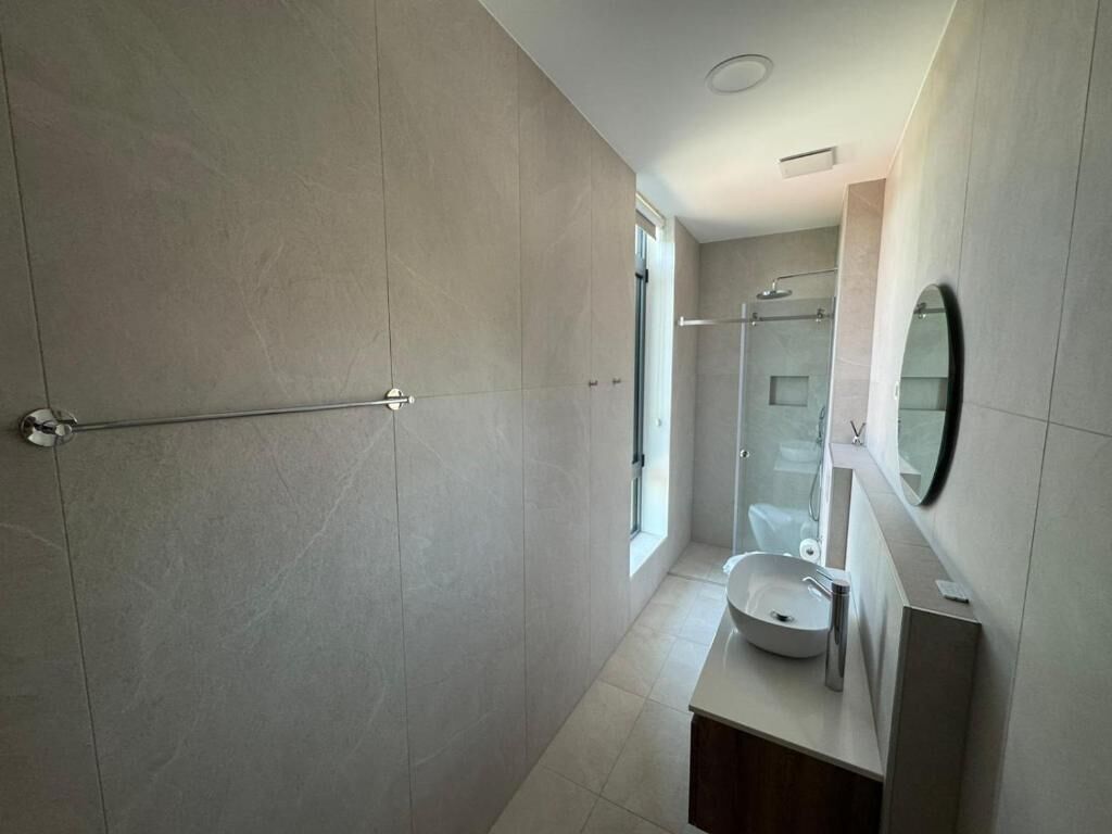 A modern bathroom with a glass shower enclosure, a sink with a mirror, and a towel rack.