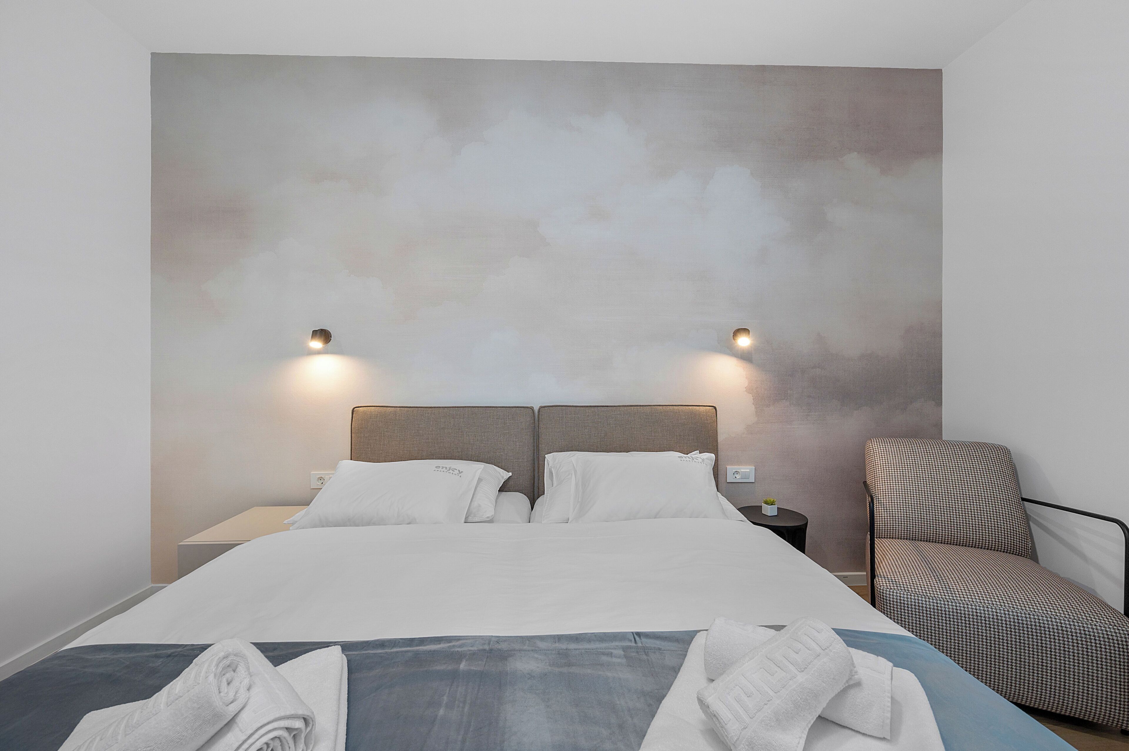 A modern hotel room with a large bed, two bedside tables, and a chair.