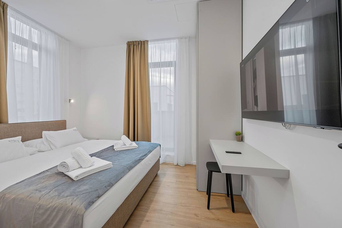 A modern hotel room with a bed, a desk, and a TV.