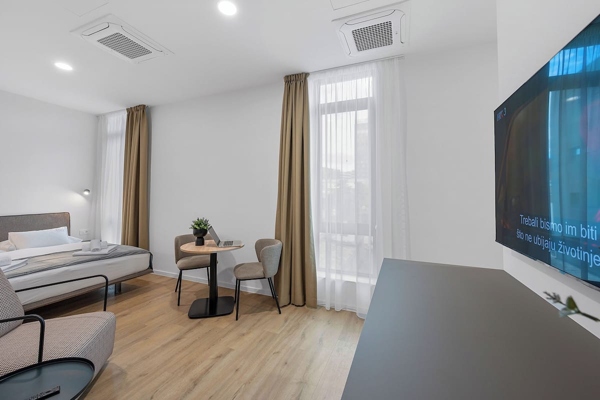A hotel room with a bed, a desk with a laptop, a chair, and a TV on the wall.