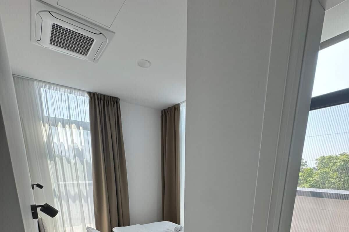 A modern hotel room with a bed, a small round table, a black trash bin, and a view of the outside.