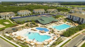 Een resort met meerdere gebouwen, een groot zwembad, tennisbanen en een aangelegde tuin met parasols.
