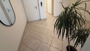 A hallway with a tiled floor, a potted plant, a white door, and a wall-mounted phone.