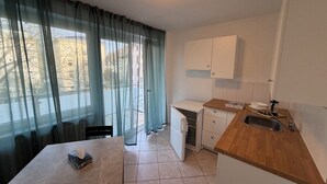 A compact kitchen with a wooden countertop, a sink, and a small refrigerator. A dining table with a box and a tissue is visible.