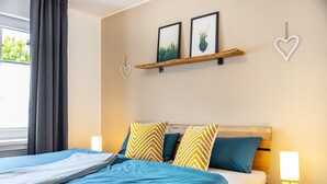 Cama bem arrumada com roupa de cama azul, cabeceira de madeira e dois quadros pendurados na parede.