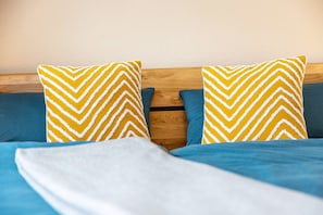 Un lit avec une literie bleue et deux oreillers jaunes ornés de chevrons blancs.