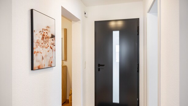 Um corredor com uma porta preta, um quadro na parede e chão de madeira.