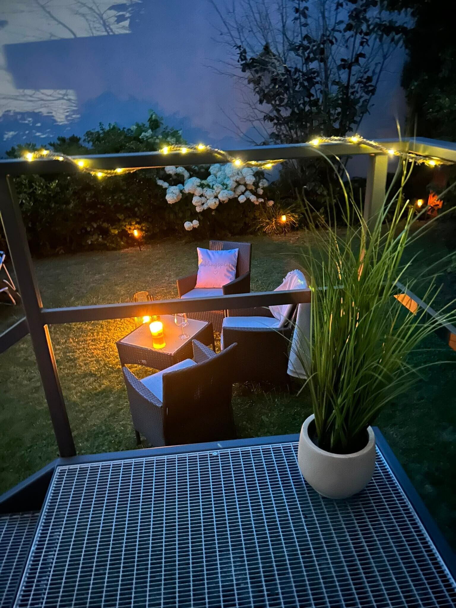 An outdoor seating area with wicker furniture, a potted plant, and string lights.