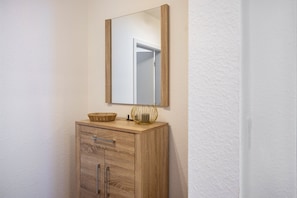 Un meuble en bois avec un miroir au-dessus, un panier et un petit vase posé sur le meuble.