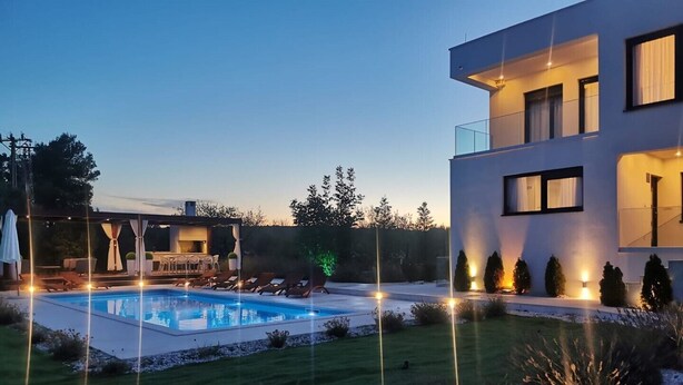 Una casa moderna de dos pisos con piscina, mobiliario exterior y jardinería iluminada.