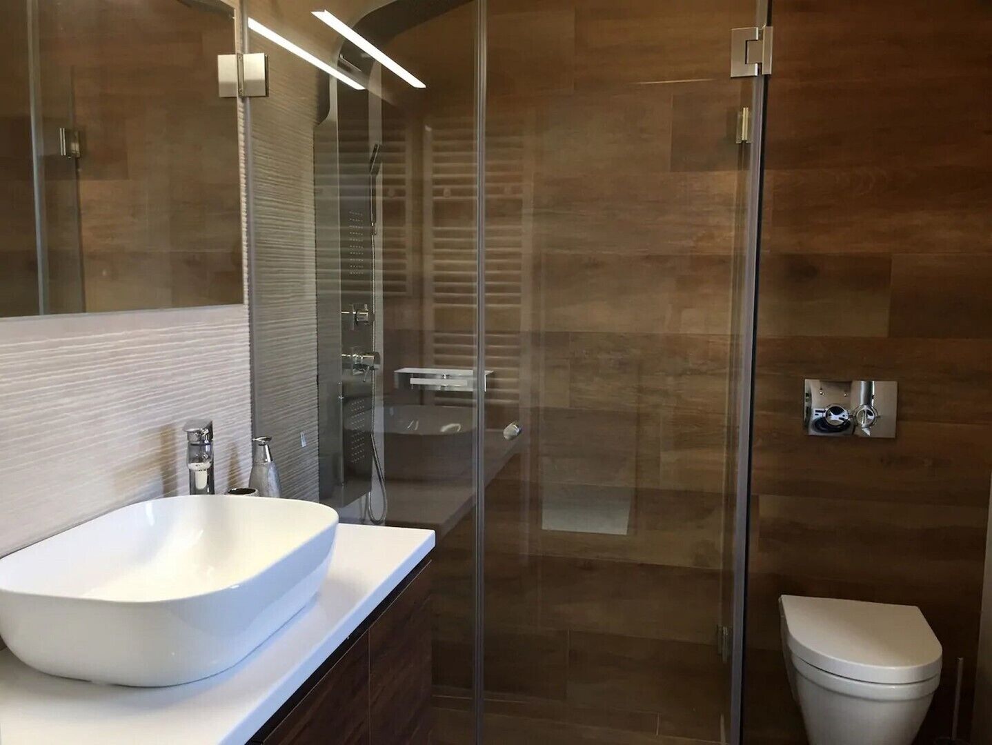 A modern bathroom with a glass shower enclosure, a white sink, and a toilet.