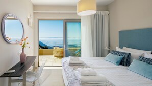 Un dormitorio con cama, escritorio, silla, un jarrón con flores, espejo y vista al exterior.