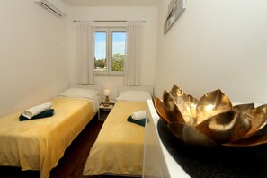 Ein Hotelzimmer mit zwei Betten, einem Fenster mit Vorhängen, einer Klimaanlage und einem goldenen Dekorationsobjekt auf einem Tisch.