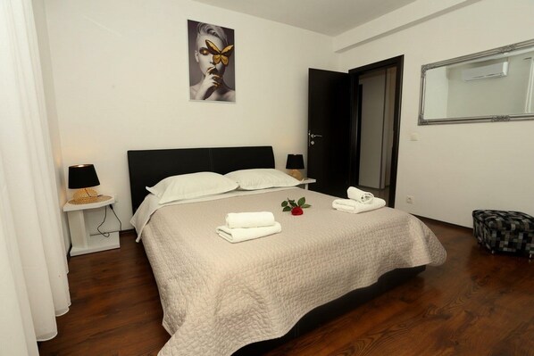 Quarto com cama, duas mesas de cabeceira, espelho, porta e um banquinho.