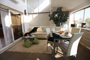A modern living room with a sofa, coffee table, and dining area. There is a sliding glass door leading to a balcony. - Villa Ombre in Okrug Gornji (Okrug Gornji)