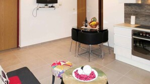 A modern kitchen with a dining area, a flat-screen TV mounted on the wall, and a small round table with decorative items. - Two Bedroom Apartment with Shared Pool (Arbanija)
