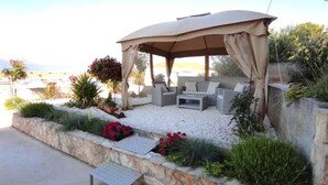 An outdoor seating area with a canopy, stone walls, and potted plants. - Two Bedroom Apartment with Shared Pool (Arbanija)