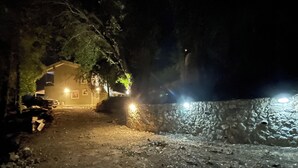 Een nachtscène met een stenen muur en een gebouw met verlichte ramen.