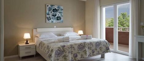 A bedroom with a bed, two bedside tables, a nightstand, a large window with a view, and a ceiling light.