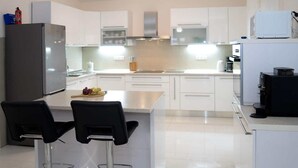 Une cuisine moderne avec des meubles blancs, un réfrigérateur en acier inoxydable, une machine à café et deux tabourets de bar.