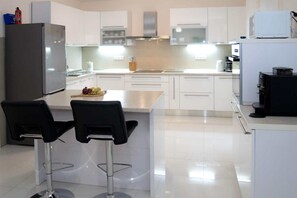 A modern kitchen with white cabinets, a stainless steel refrigerator, a coffee machine, and two bar stools. - Four Bedroom Villa with Pool (Lećevica)