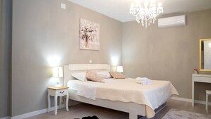 Une chambre à coucher avec un lit, des tables de chevet, un lustre, un tableau et un miroir.