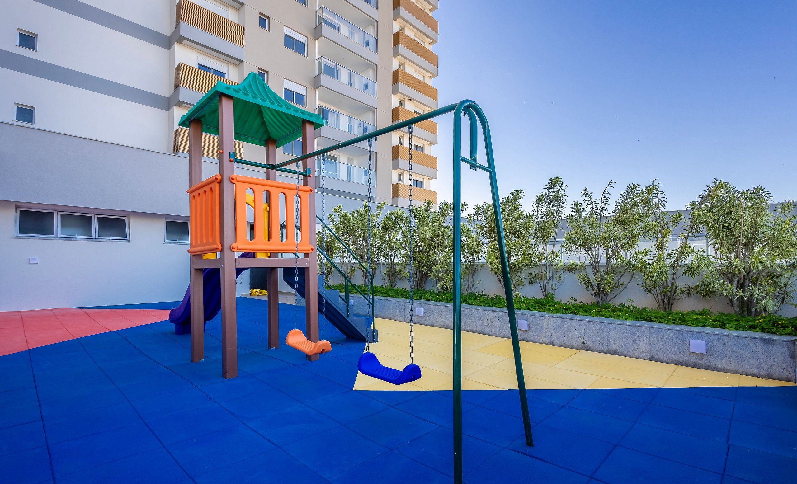 A playground with a slide and swings, surrounded by a building with balconies.