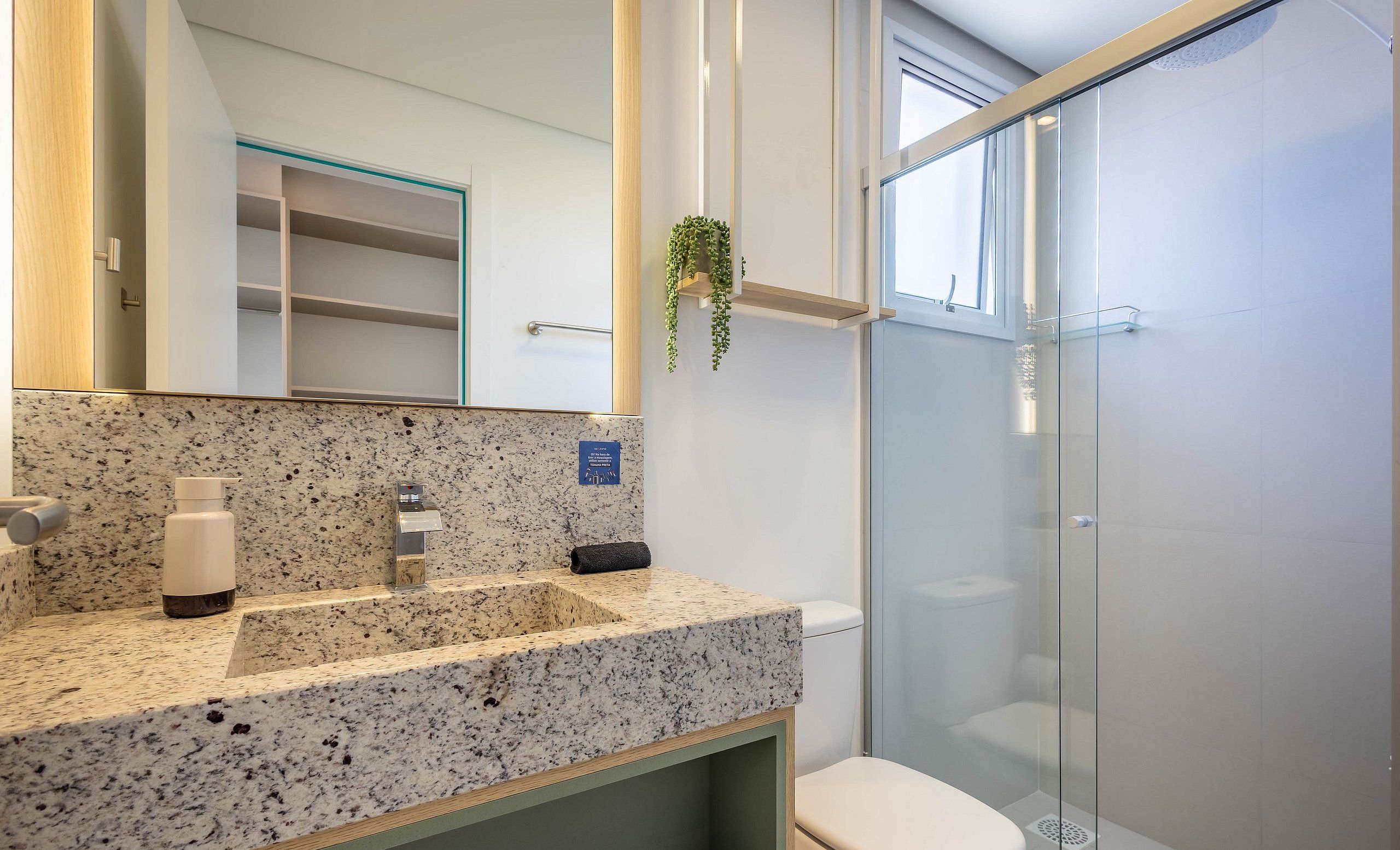 A bathroom with a granite countertop, a mirror, a towel rack, and a glass-enclosed shower.