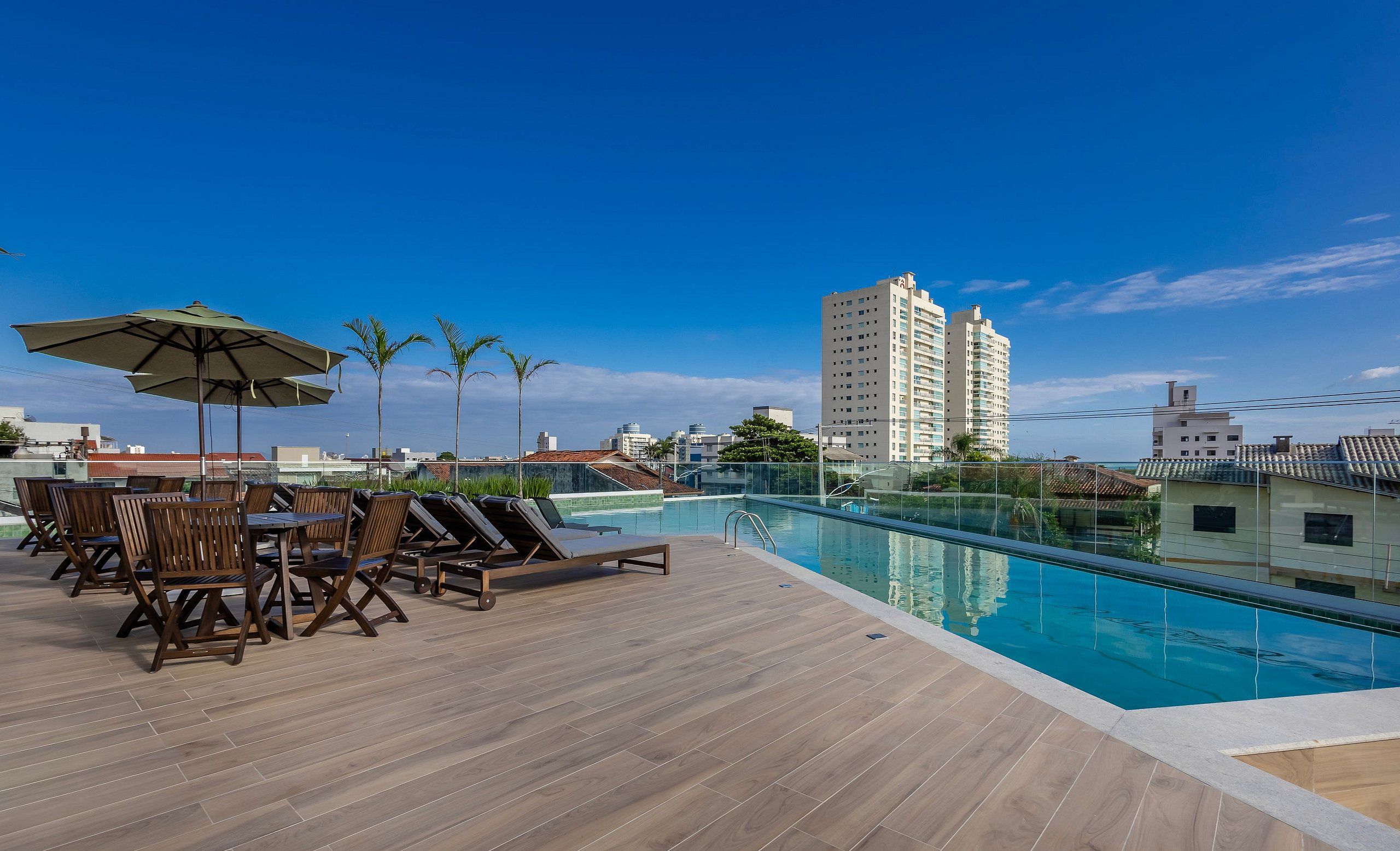 A rooftop pool area with lounge chairs and umbrellas, surrounded by tall buildings.