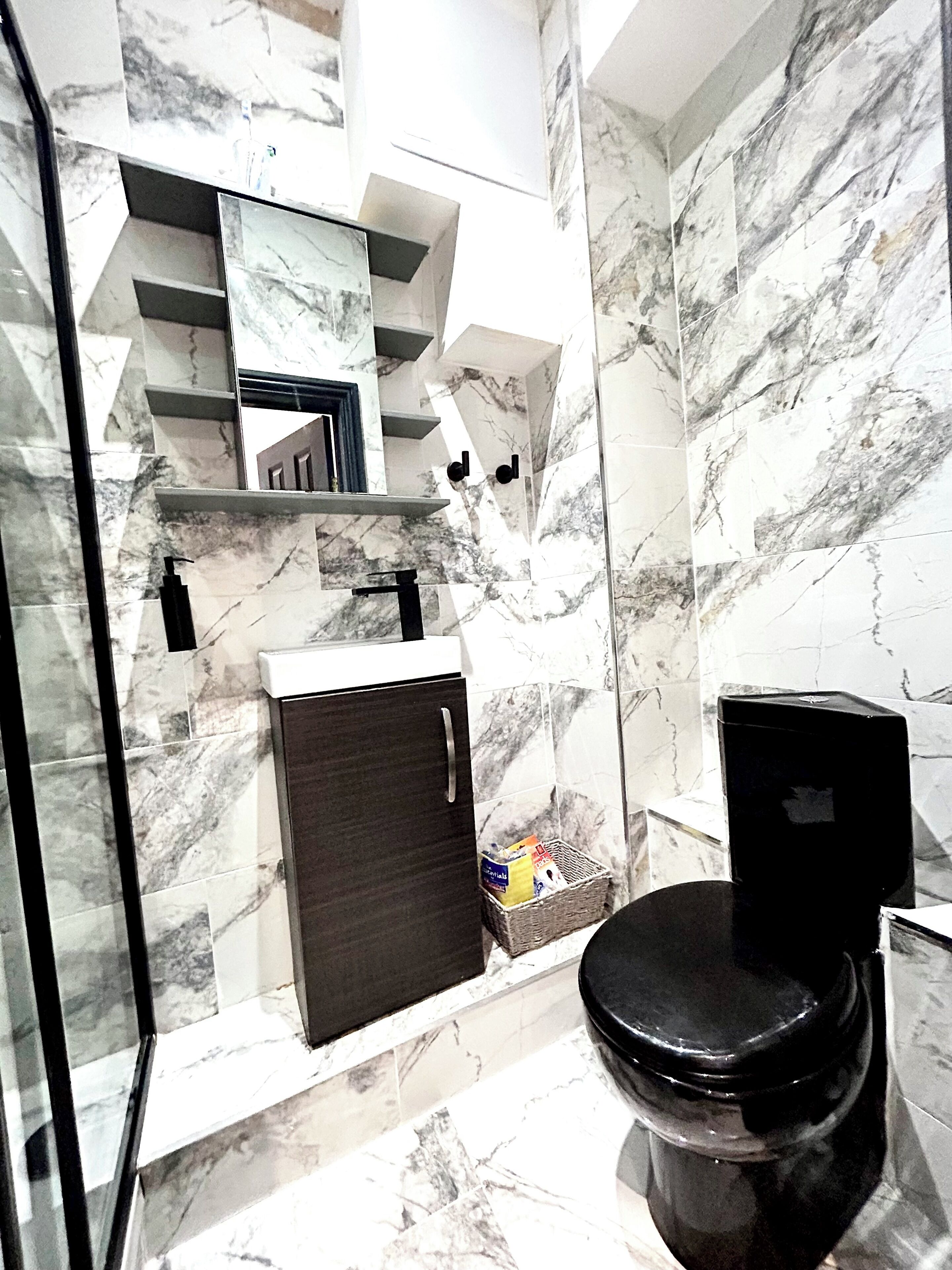 A bathroom with marble walls, a black toilet, a small sink, and a mirror above the mirror cabinet.