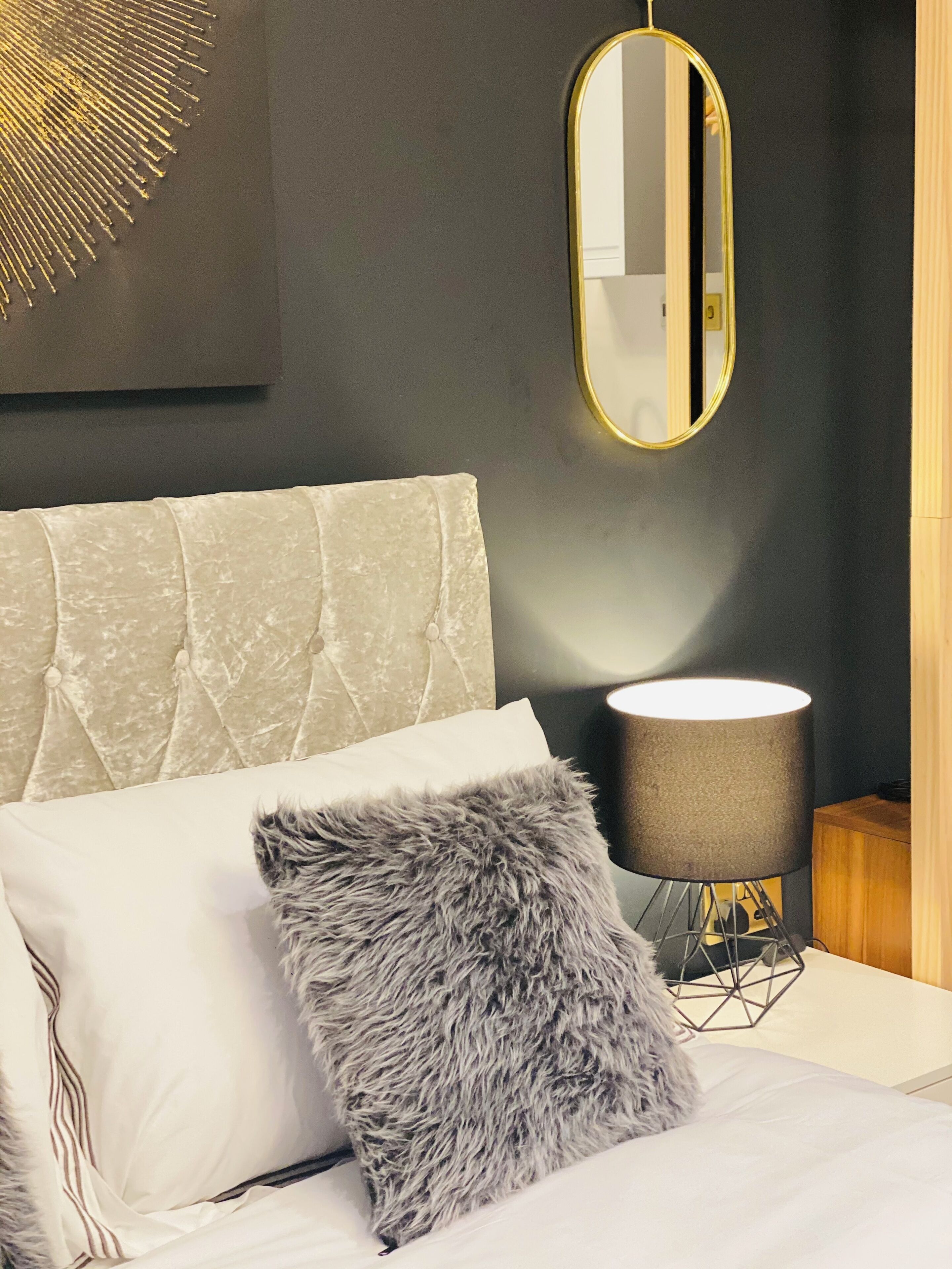 A bed with a tufted headboard, a fluffy pillow, and a bedside lamp.