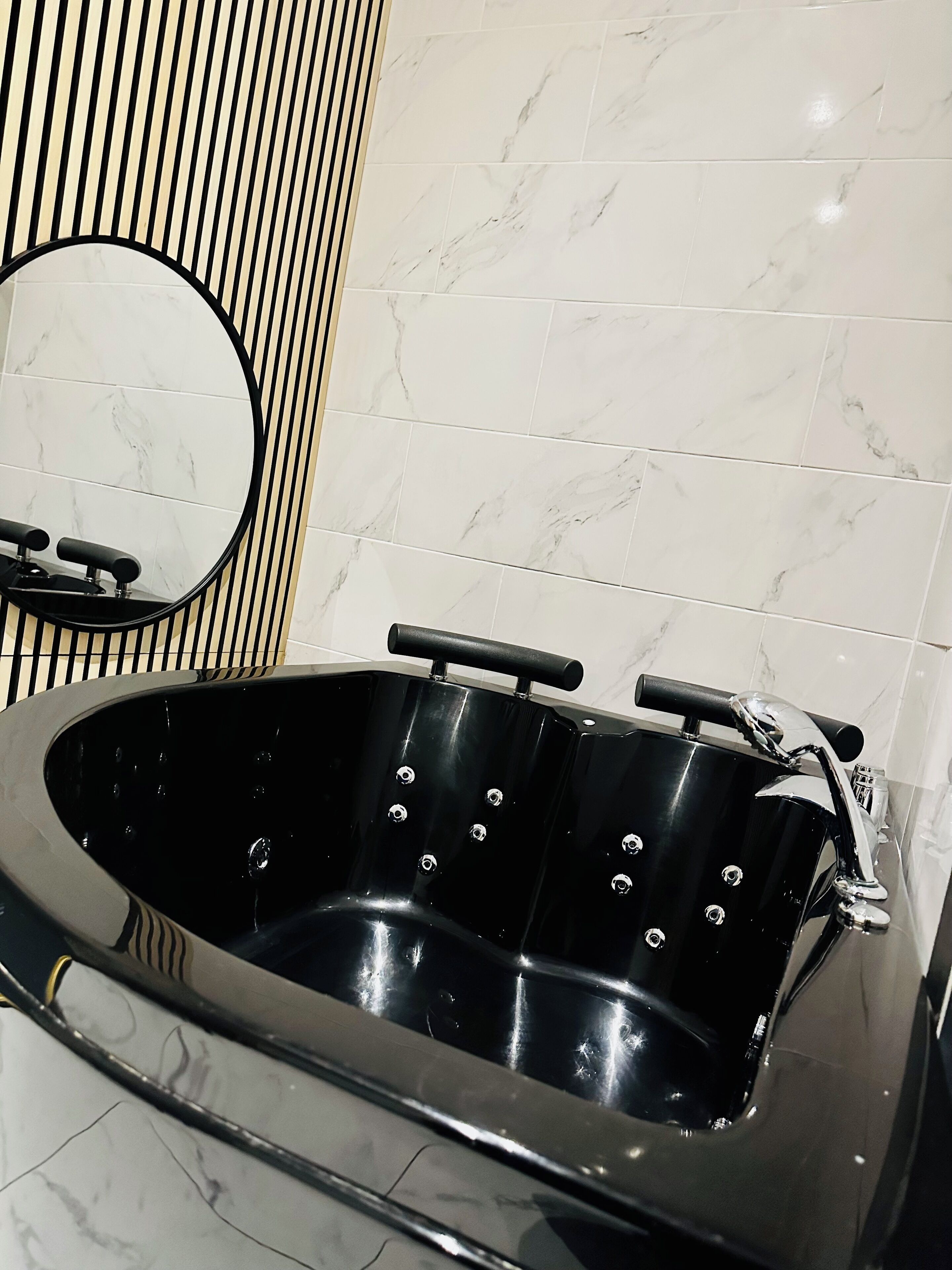 A black jacuzzi tub with a round mirror and a black towel rack.