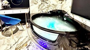 A bathroom with a marble wall, a bathtub with blue LED lights, a small blue chair, and a television on the wall. - BPR Private Hot-tubs and rooms  (London)