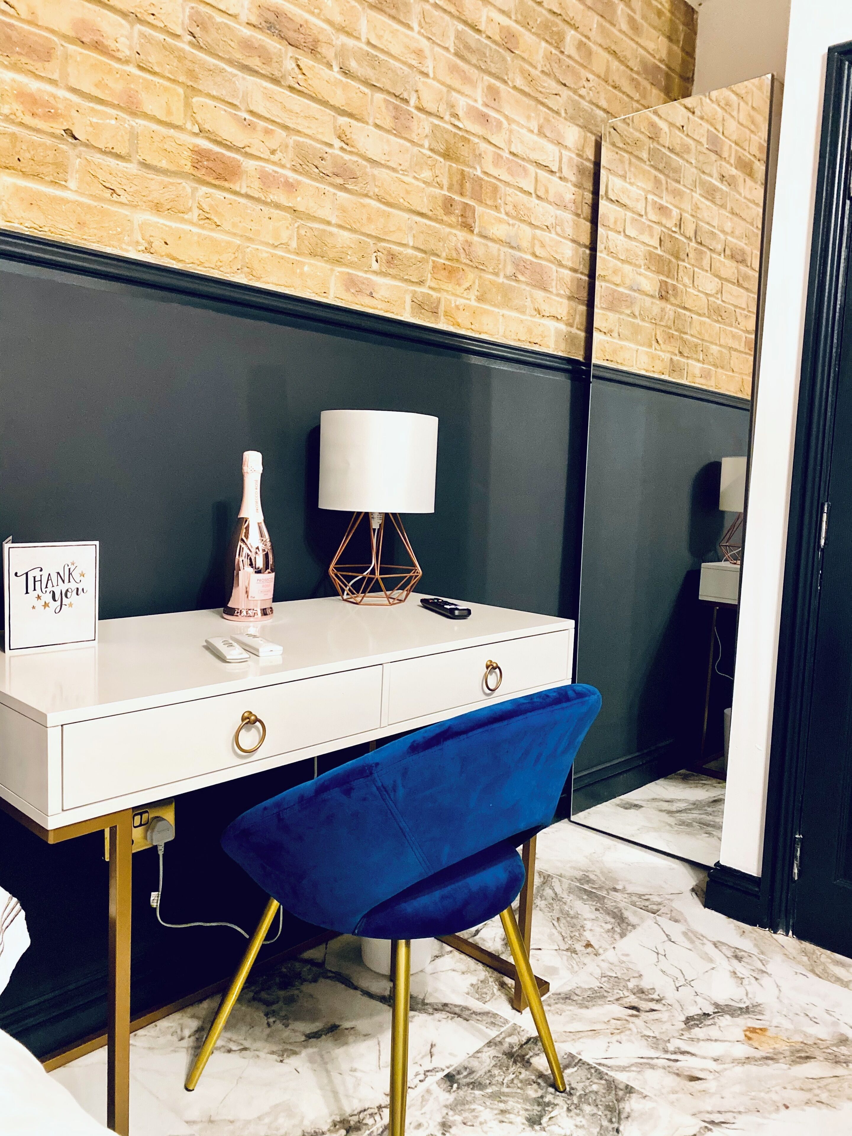 A white desk with a blue chair, a lamp, and a thank you card.