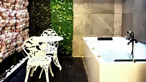 A bathroom with a white bathtub, a small table with chairs, and a green vertical garden. - BPR Private Hot-tubs and rooms  (London)