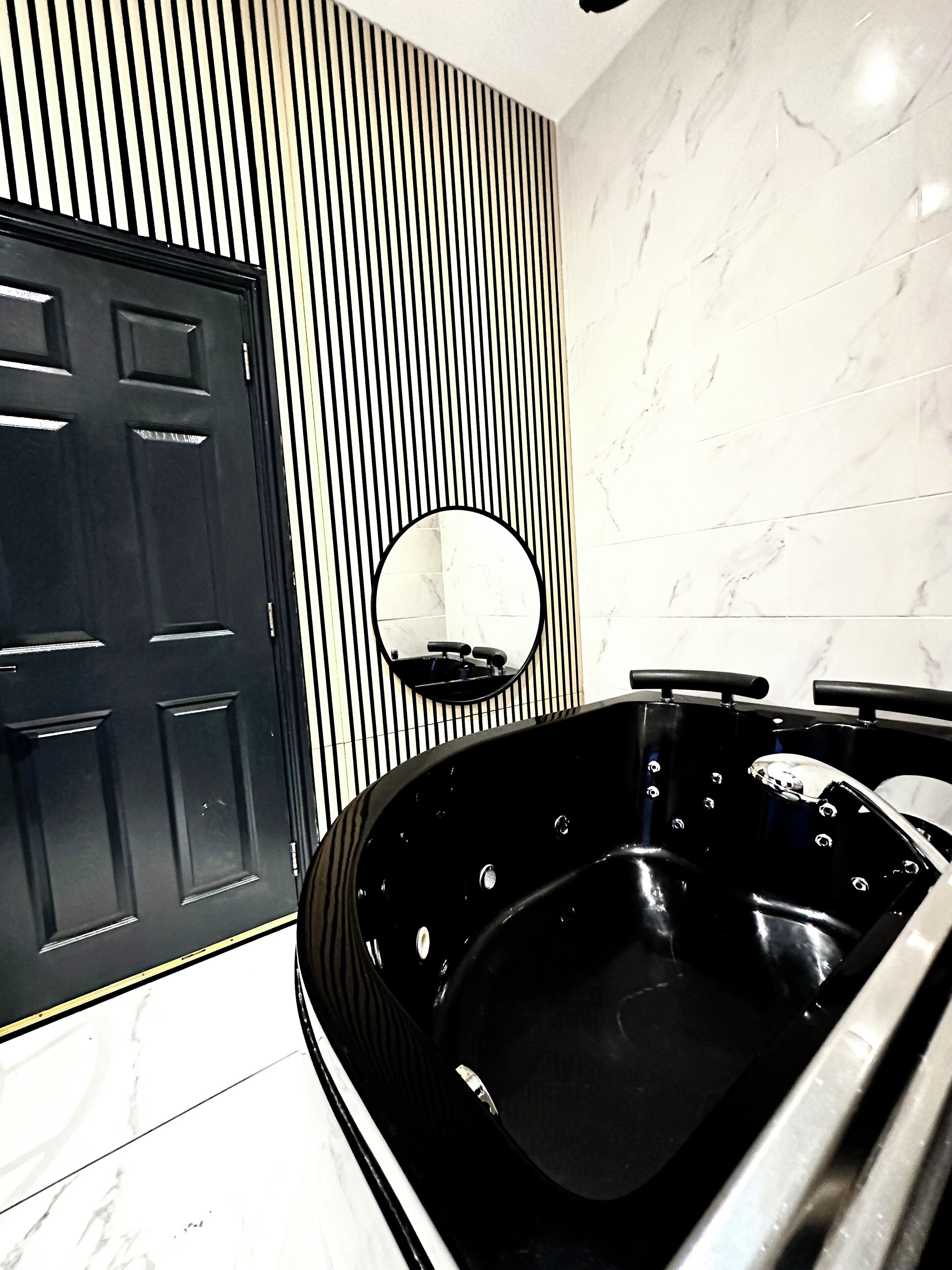 Une salle de bain moderne avec une baignoire noire, une porte noire et un miroir au mur.