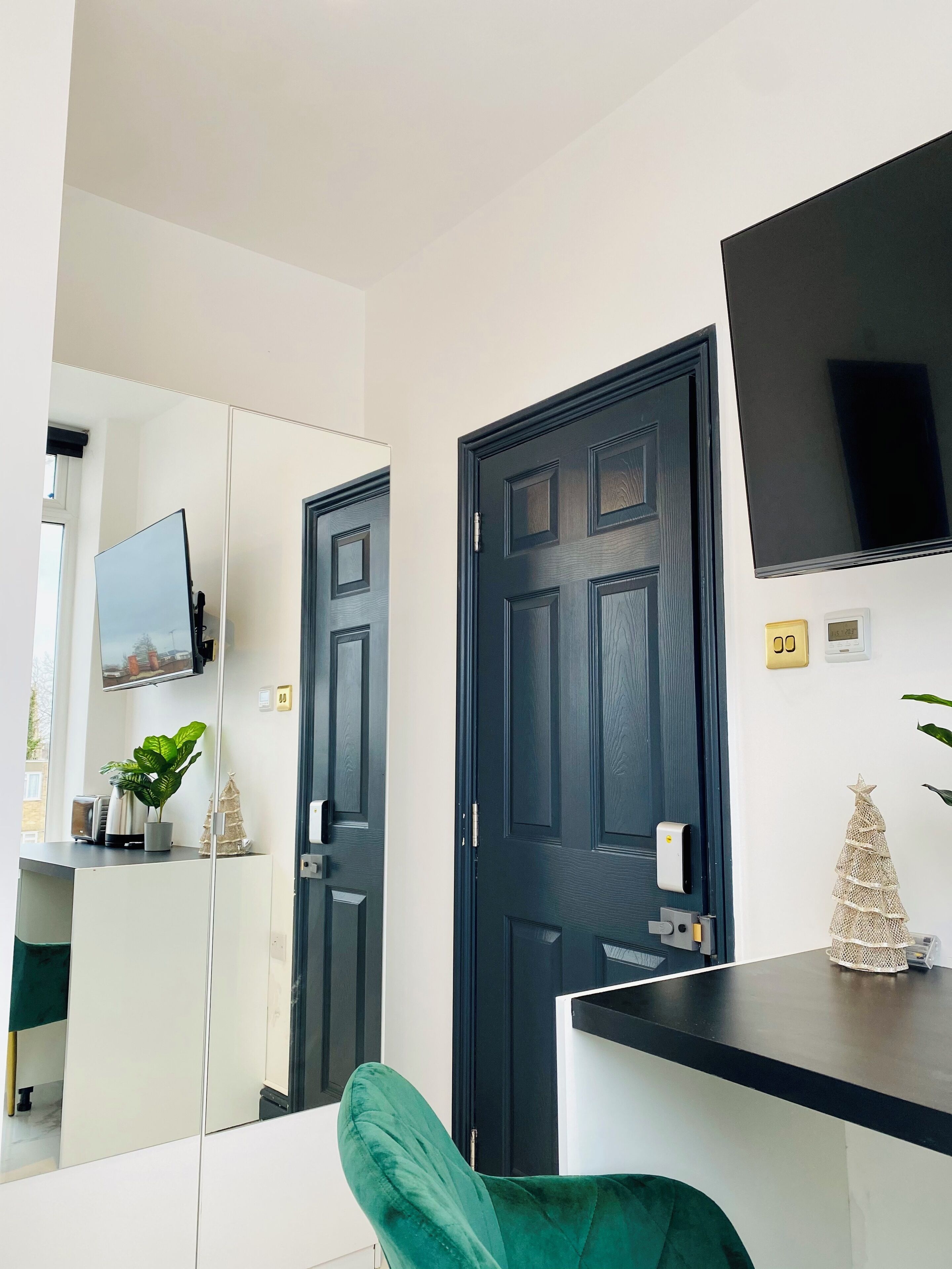 A modern room with a large mirror, a flat-screen TV, a dark wooden door, and a small Christmas tree decoration.