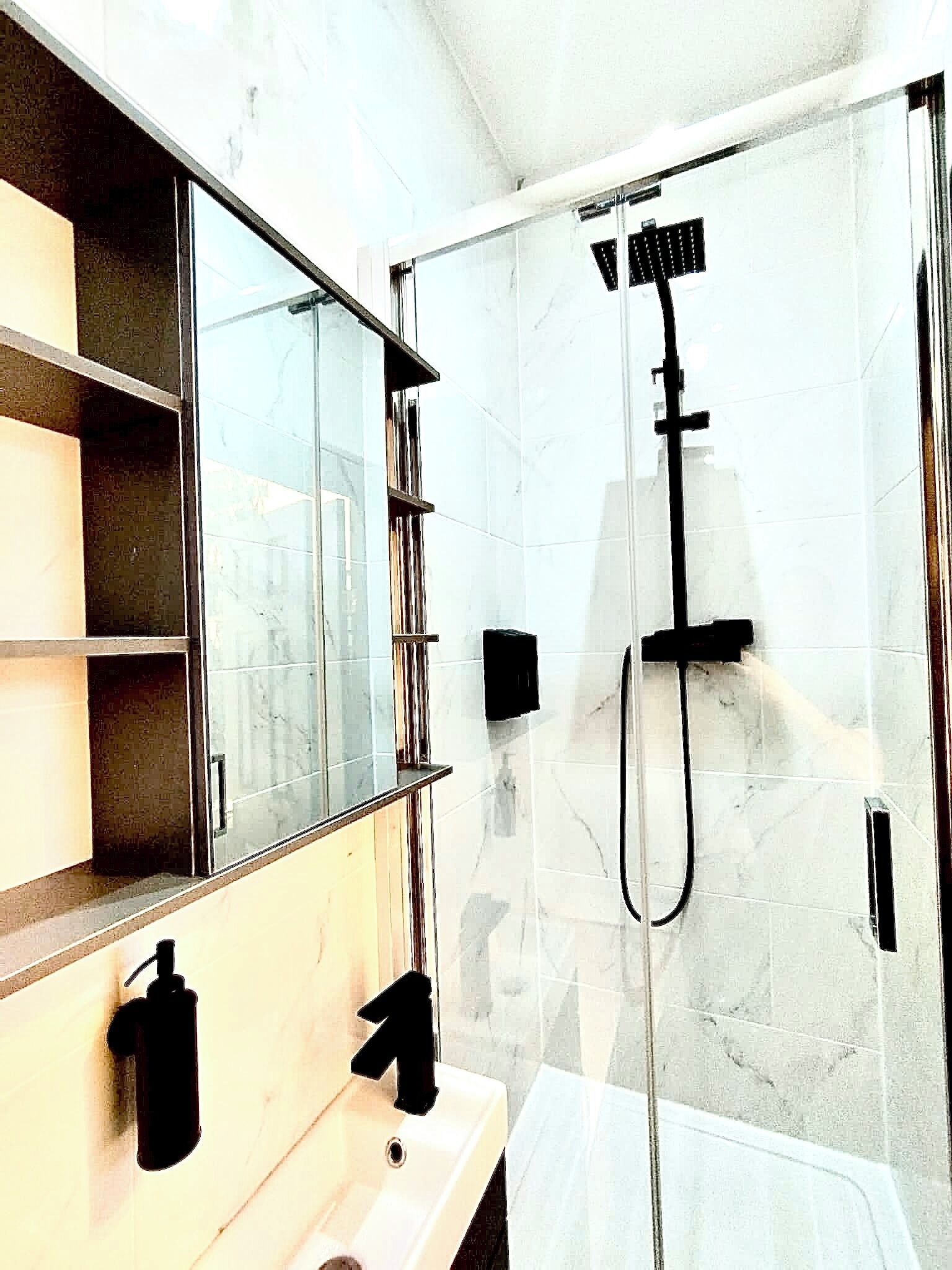 A modern bathroom with a glass-enclosed shower, a large mirror, and a vanity with a sink.