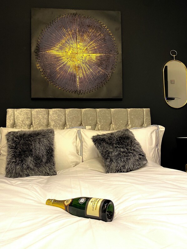 Una cama con dos almohadas mullidas, una botella de champán y una obra de arte en la pared.