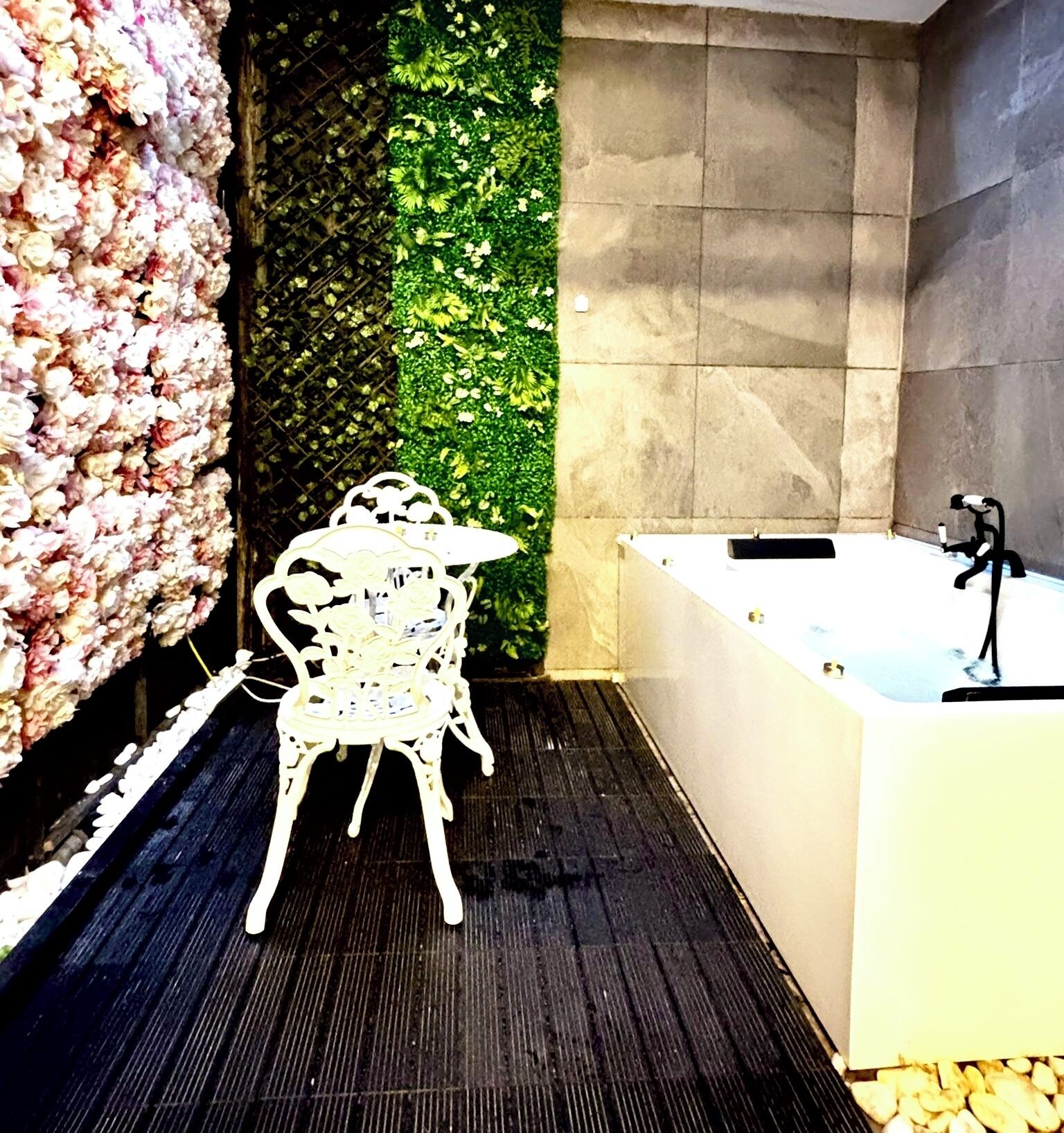 Un baño moderno con una bañera grande, una silla blanca y un jardín vertical verde.
